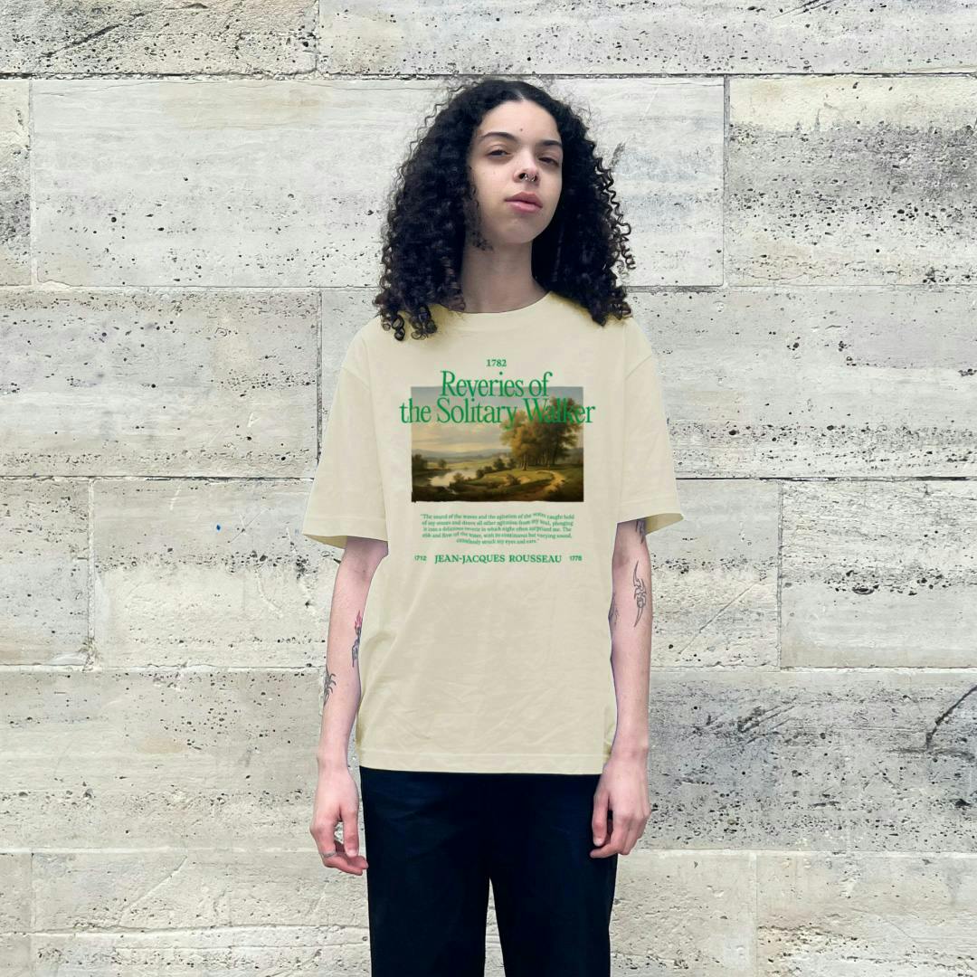 A woman with long dark hair wearing a cream-colored short-sleeved shirt with a landscape painting and green text above it, and a quote below it. 